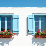 Façade d'une maison méditerranéenne avec volets bleus fermés et fleurs